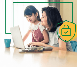 A woman and her daughter using their laptop at the dining room table. There's a green line that links to a shield icon in the background.